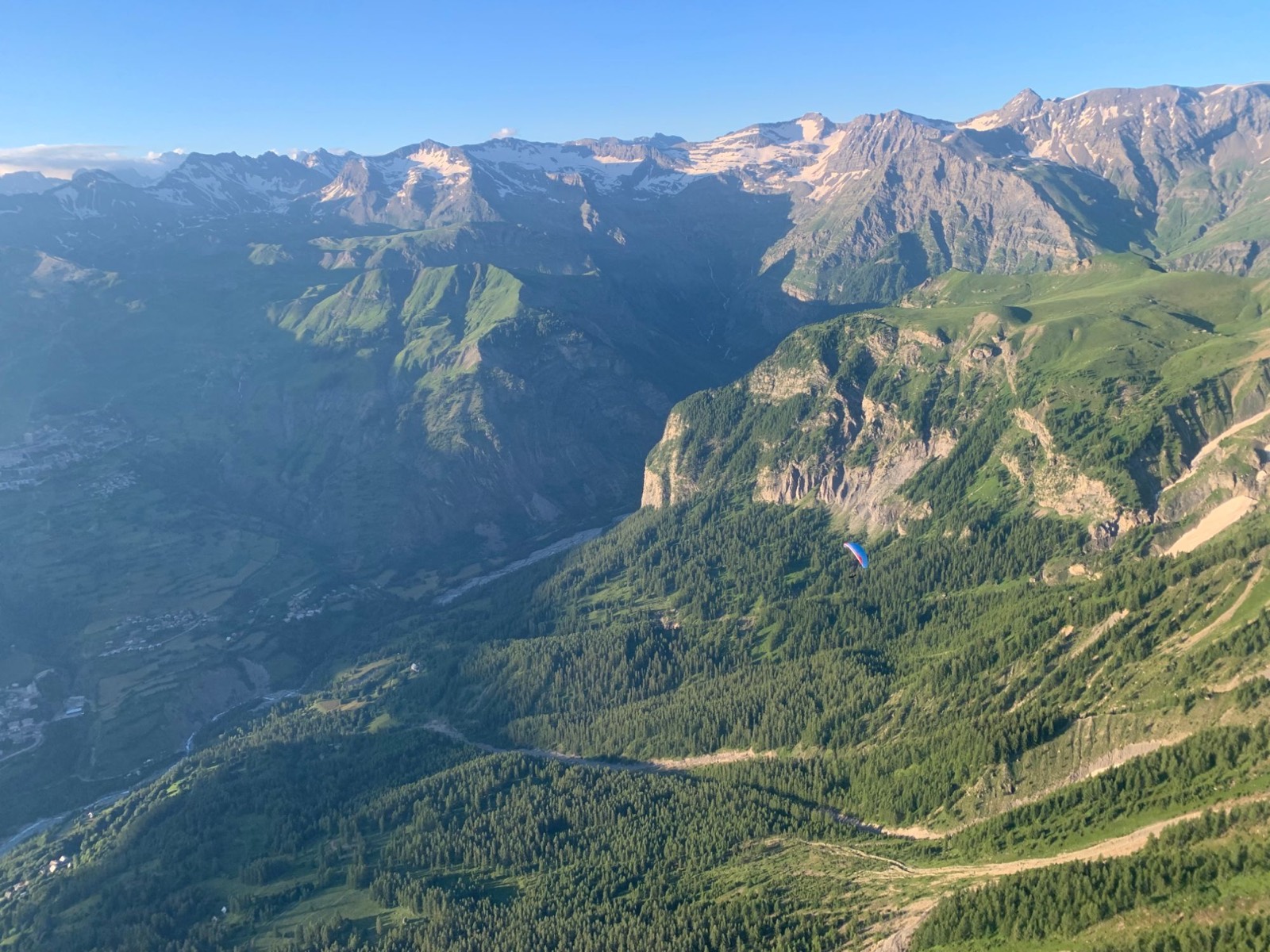 Parapente en vol dans une vallée face aux sommets enneigés