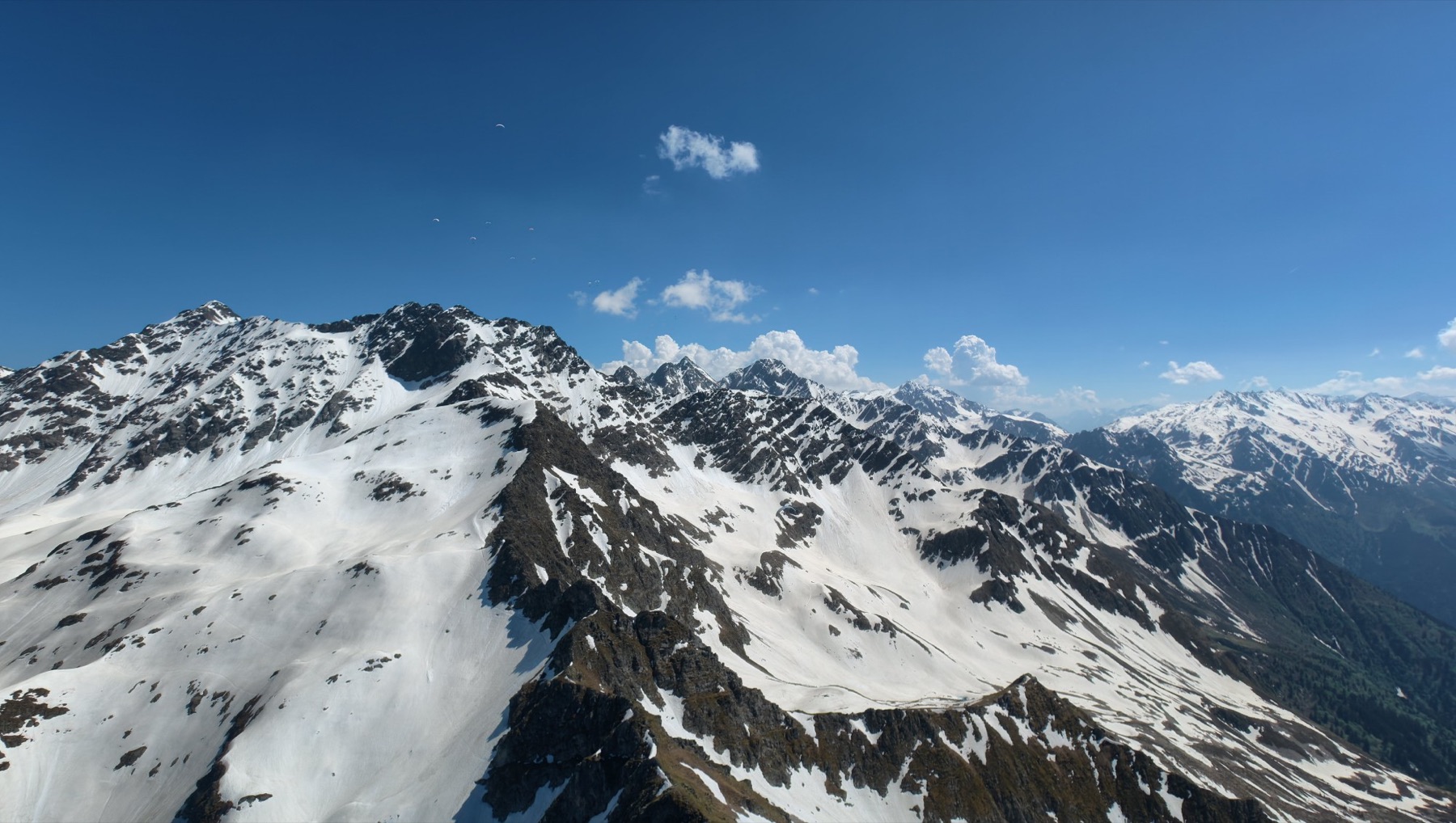 Crêtes et versants enneigés vus du ciel, avec plusieurs parapentes au loin